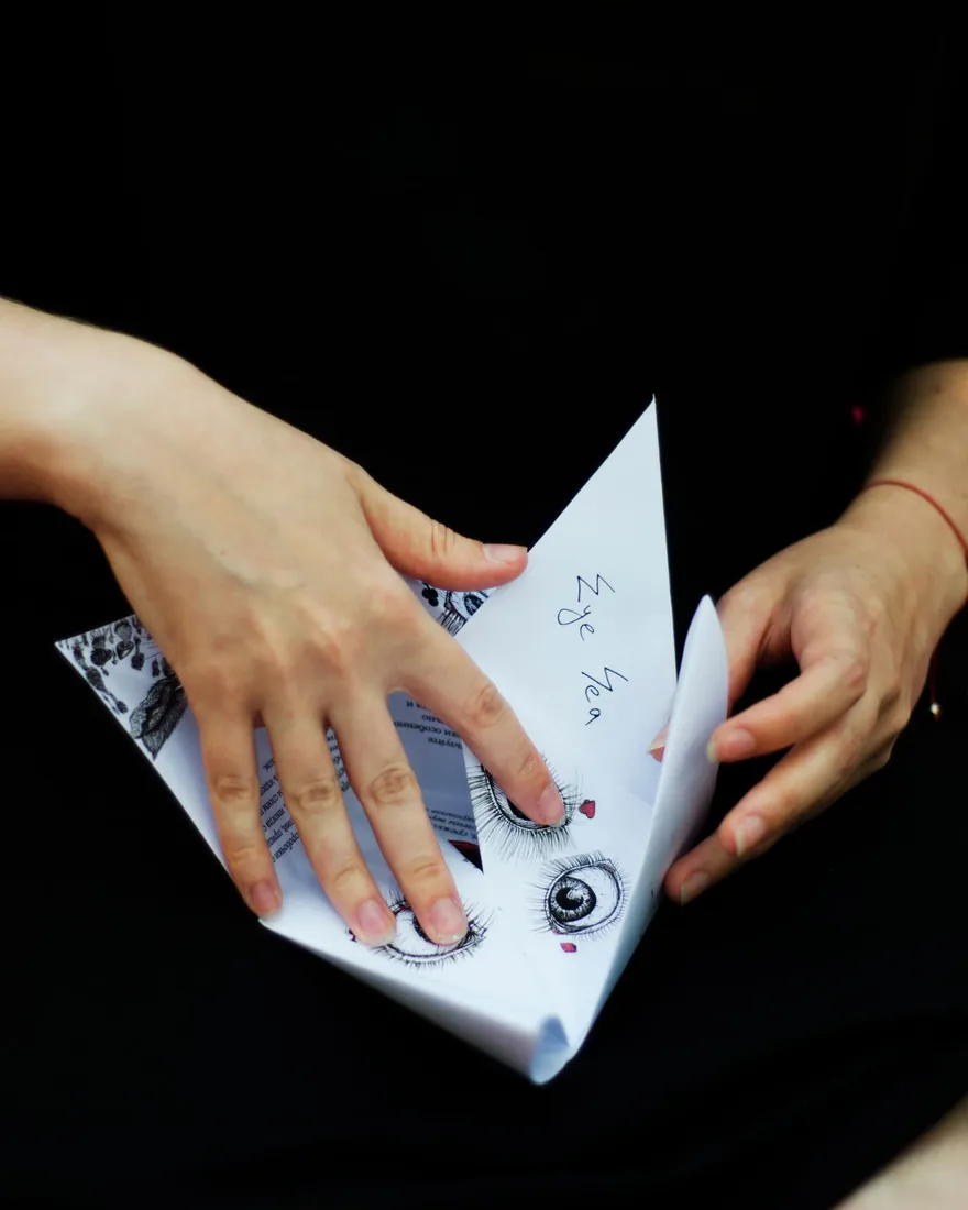 Manos plegando con cuidado una hoja de papel decorado sobre un fondo oscuro